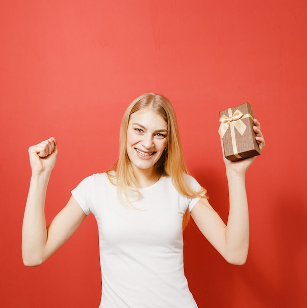 Happiness on the face of a blonde girl with a gift in her hand on a red background