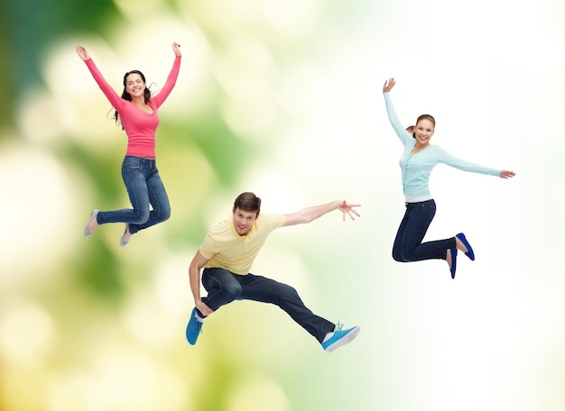幸福、自由、エコロジー、友情と人々の概念-緑の背景の上に空中でジャンプする笑顔のティーンエイジャーのグループ
