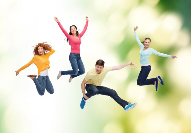 幸福、自由、エコロジー、友情と人々の概念-緑の背景の上に空中でジャンプする笑顔のティーンエイジャーのグループ