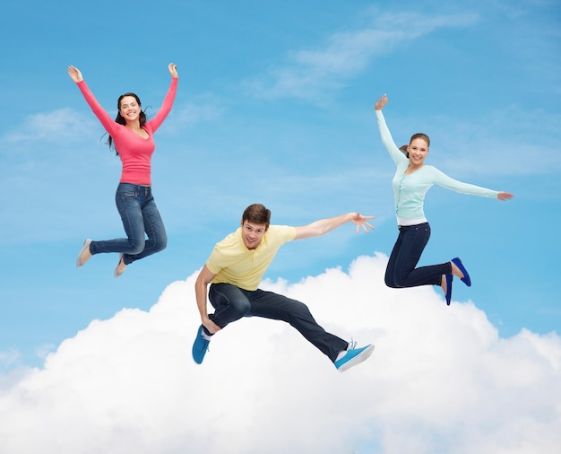 幸福、自由、友情、動きと人々の概念-白い雲の背景と青い空の上を空中でジャンプする笑顔のティーンエイジャーのグループ