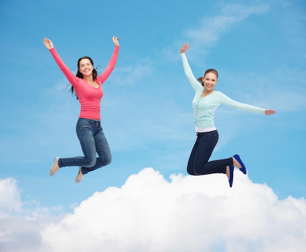 happiness, freedom, friendship, movement and people concept - smiling young women jumping in air over blue sky with white cloud background