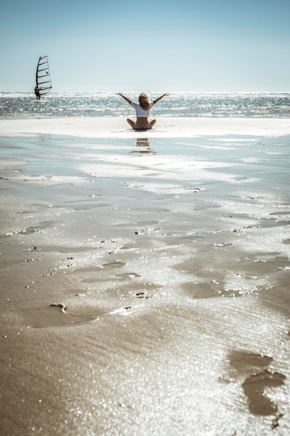 Concetto di stile di vita di felicità e libertà vista posteriore di una donna seduta sulla sabbia con l'oceano intorno alle braccia aperte con soddisfazione e gioia persone di sesso femminile che si godono la destinazione delle vacanze estive