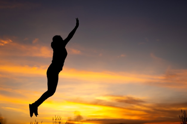 幸福、自由、動きと人々の概念-空中夕日の背景にジャンプする笑顔の若い女性