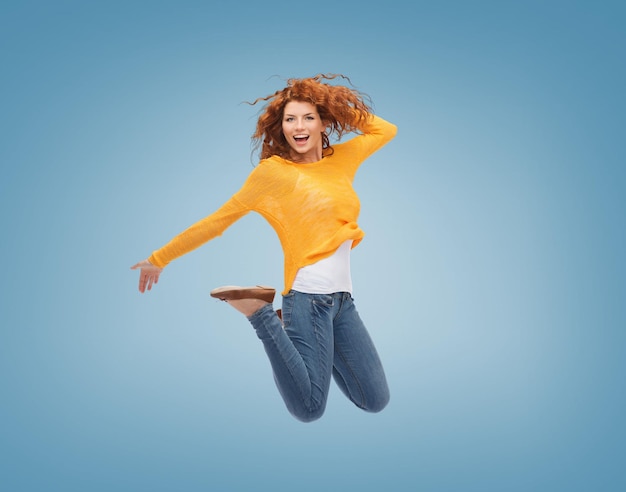 행복, 자유, 운동, 그리고 사람들의 개념 - 파란 배경 위에서 공중으로 점프하는 웃고 있는 젊은 여성