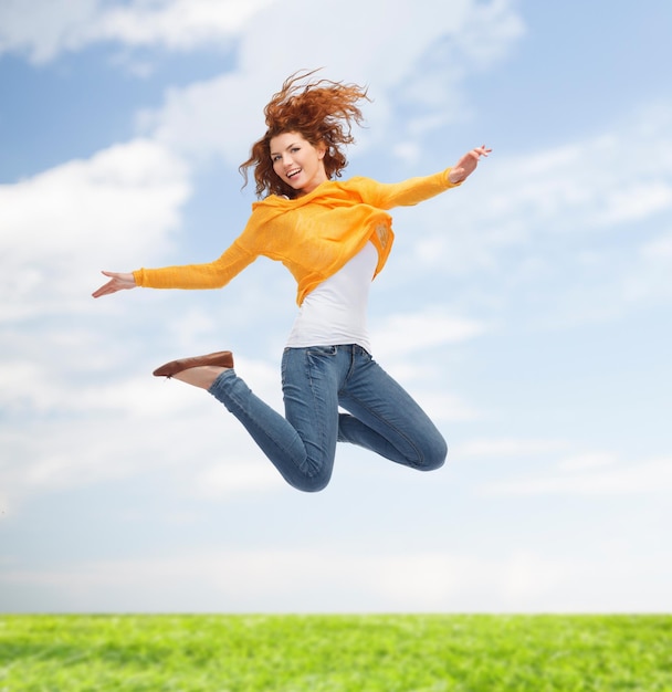 happiness, freedom, movement and people concept - smiling young woman jumping high in air over green background over blue sky and grass background