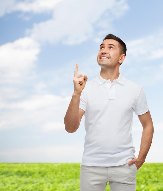 행복, 제스처 및 사람 개념 - 푸른 하늘과 잔디 배경 위에 손가락을 가리키는 웃는 남자