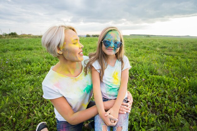 Felicità, festival di holi e concetto di vacanze - madre e figlia ricoperte di polvere colorata