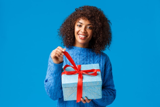 Felicità, vacanze e concetto di famiglia. donna afroamericana affascinante sorridente felice con taglio di capelli afro, regalo da scartare, tirando nodo e presente di ricezione allegro sorridente sul nuovo anno