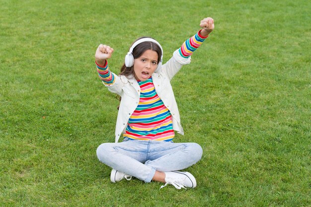 Happiness is not something you sit back and wait. listen music\
while relaxing outdoor. child headphones listen music. cool girl\
headphones listening music. kid girl enjoy music green grass\
meadow.