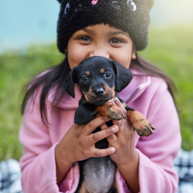 행복은 꿈틀거리는 강아지입니다. 밖에 앉아 있는 동안 강아지를 껴안고 있는 귀여운 소녀의 자른 초상화