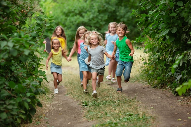 Happiness. Kids, children running on green forest. Cheerful and happy boys and girs playing, laughting, running through green blooming meadow. Childhood and summertime, sincere emotions concept.