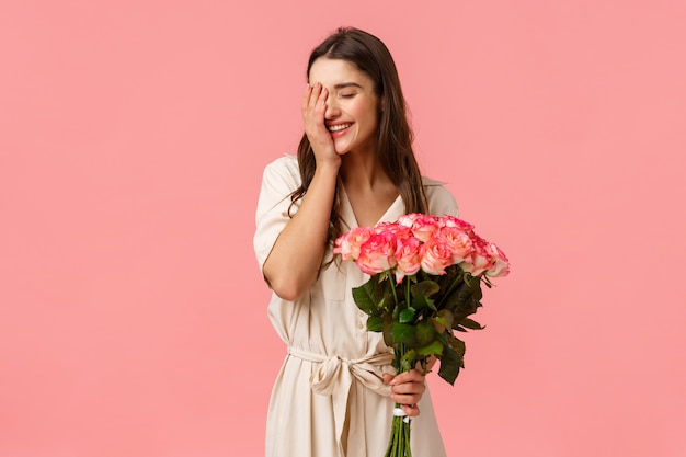 Happiness, love and relationship concept, Woman feeling cherished and valued, attractive brunette girl in stylish dress, holding roses, flower bouquet and smiling, laughing shy, pink 