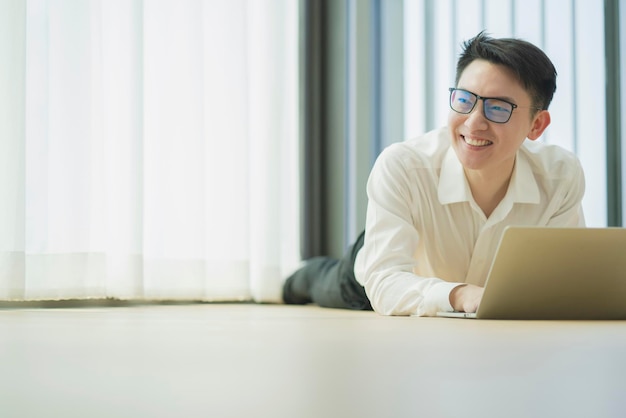 Happiness peaceful smile asian male enjoy work from home
quarantine relax and positive work with laptopasian male attractive
smart freelance lay down use laptop on laminate wooden floor