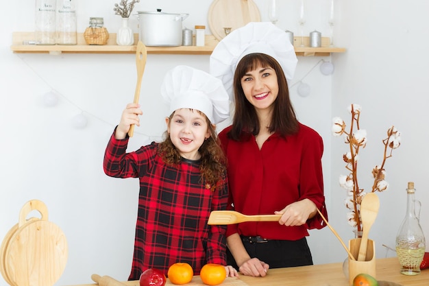 幸せと人々の概念白いキッチンで生地を作るシェフの帽子のママと子供