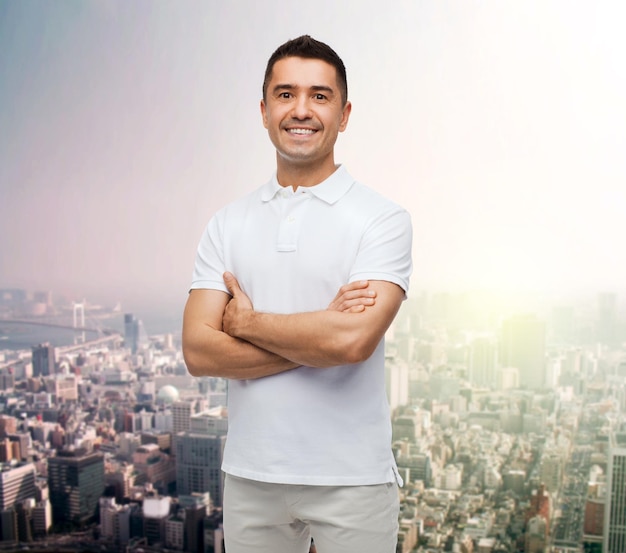 концепция счастья и людей - улыбающийся мужчина в белой футболке со скрещенными руками на фоне города