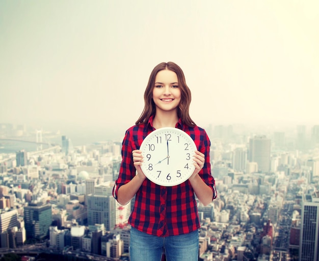 happiness and people concept - smiling young woman in casual clothes with wall clock showing 8 oclock
