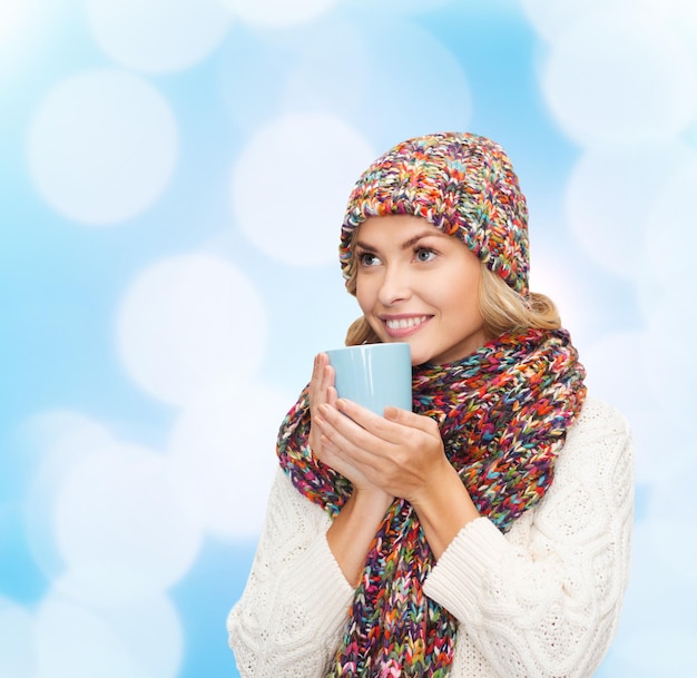 행복, 겨울 방학, 크리스마스, 음료, 그리고 사람들의 개념 - 파란 불빛 배경 위에 컵을 들고 따뜻한 옷을 입고 웃고 있는 젊은 여성