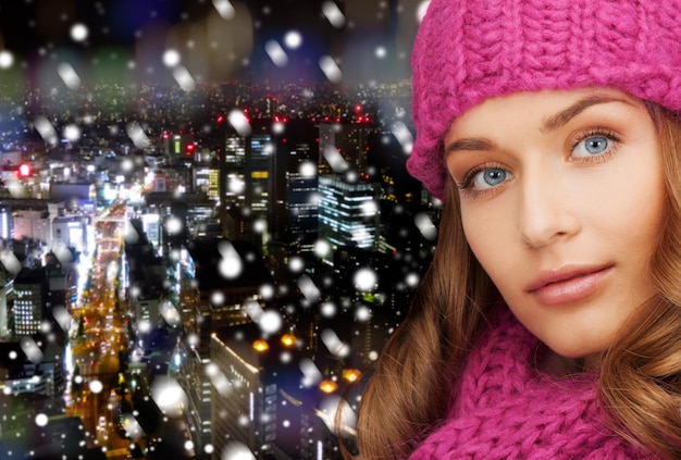 счастье, зимние каникулы, рождество и концепция людей - крупным планом улыбающаяся молодая женщина в розовой шляпе и шарфе на фоне снежного ночного города