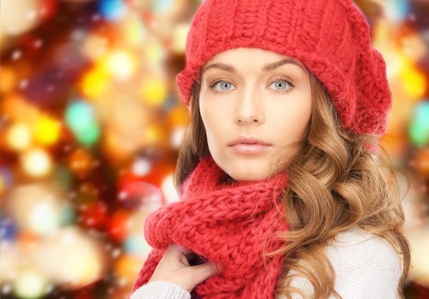 happiness, winter holidays, christmas and people concept - close up of young woman in hat and scarf over red lights background