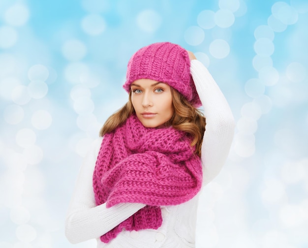 幸福、冬の休日、クリスマスと人々の概念-青い光の背景にピンクの帽子とスカーフで若い女性の笑顔