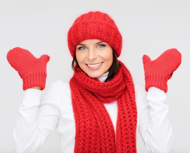 幸福、冬の休日、クリスマスと人々の概念-灰色の背景に赤い帽子、スカーフ、ミトンの笑顔の若い女性