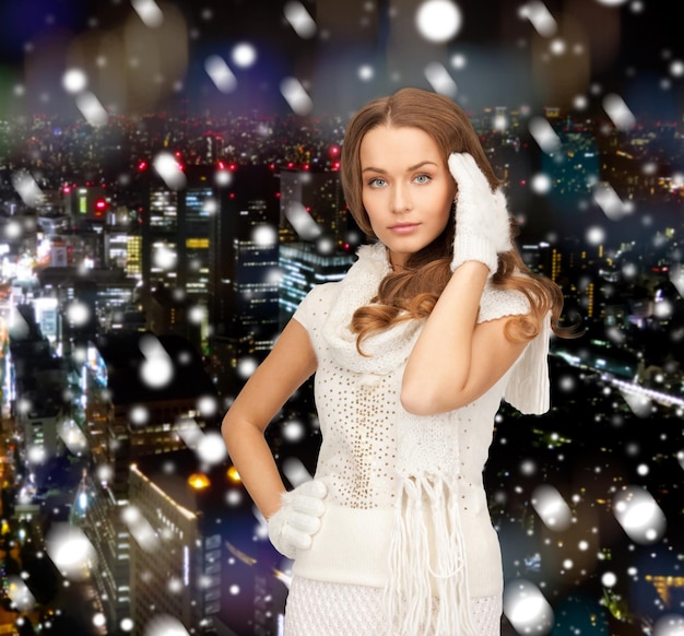 happiness, winter holidays, christmas and people concept - smiling young woman in white warm clothes over snowy city background