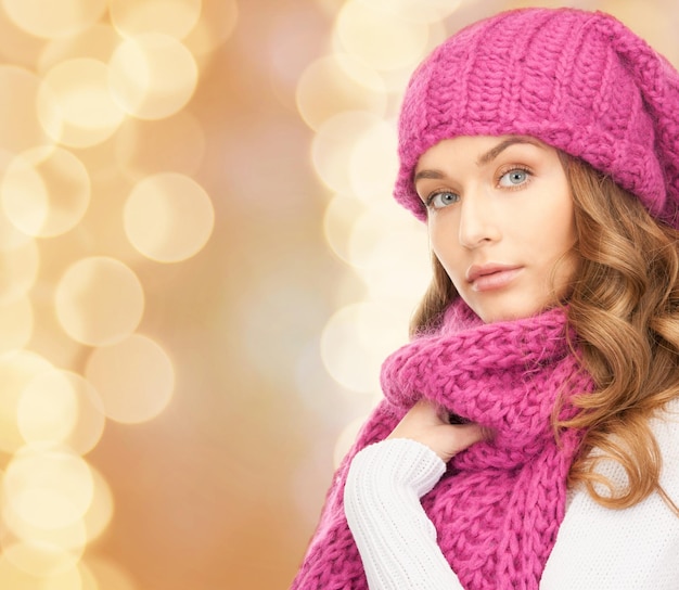 счастье, зимние каникулы, рождество и концепция людей - молодая женщина в розовой шляпе и шарфе на фоне бежевых огней