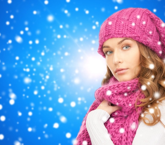 happiness, winter holidays, christmas and people concept - young woman in pink hat and scarf over blue snowy background