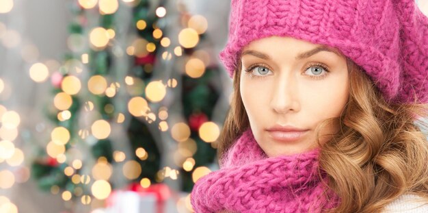 happiness, winter holidays and people concept - close up of young woman in pink hat and scarf over christmas tree lights background