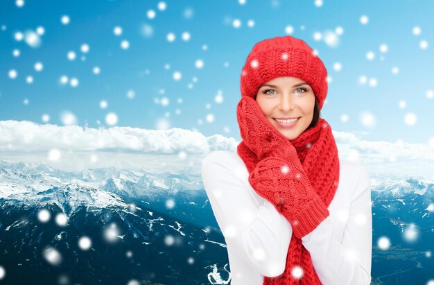 행복, 겨울 휴가, 관광, 여행, 그리고 사람들의 개념 - 눈 덮인 산 배경 위에 빨간 모자와 장갑을 끼고 웃고 있는 젊은 여성
