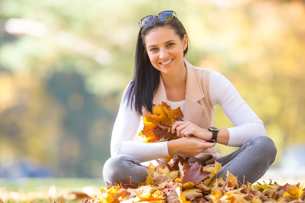 Happiness woman sitting in autumn park holding bouquet with fall leaves.