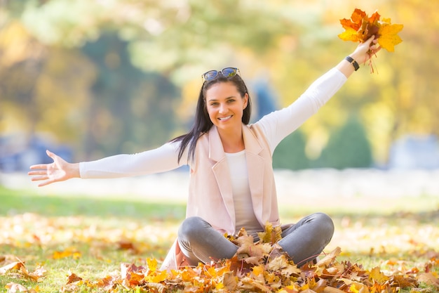 Happiness woman sitting in autumn park holding bouquet with fall leaves.