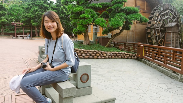 배낭을 메고 벤치에 앉아 카메라를 바라보는 행복 젊은 아시아 여성 여행자