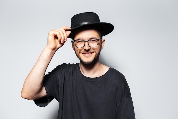 Felicità giovane ragazzo che indossa una camicia con cappello nero e occhiali da vista su sfondo grigio