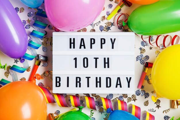 Happy 10th birthday celebration message on a lightbox with balloons and confetti