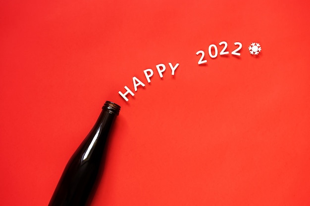 Happy 2022 lettering flies out of a bottle of champagne. Red background, New Years celebration.