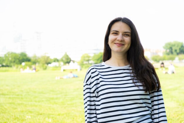 Happy 30 year old brunette woman in striped longsleeve in the park space for text