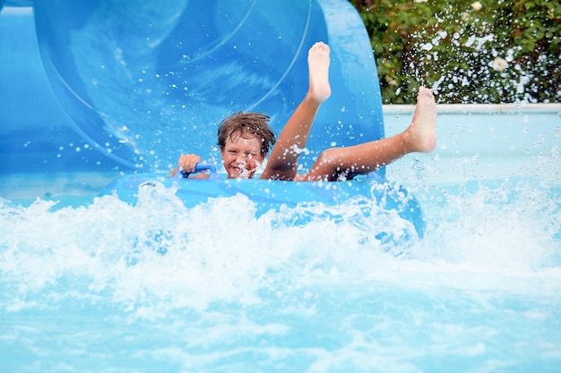 Счастливый 8-летний мальчик катается в аквапарке на надувных кругах на водных горках с брызгами