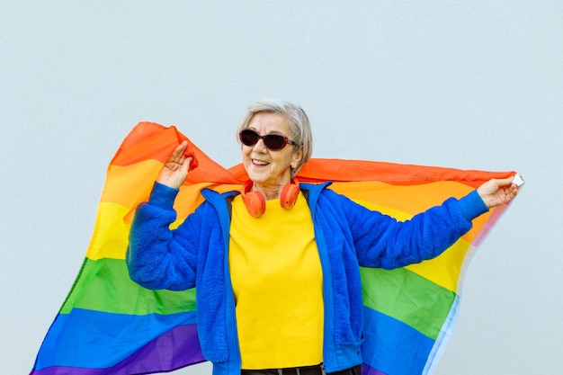 색색의 선글라스를 쓴 행복한 80세 여성이 동성애자 커뮤니티의 무지개 깃발을 자랑스럽게 흔들며