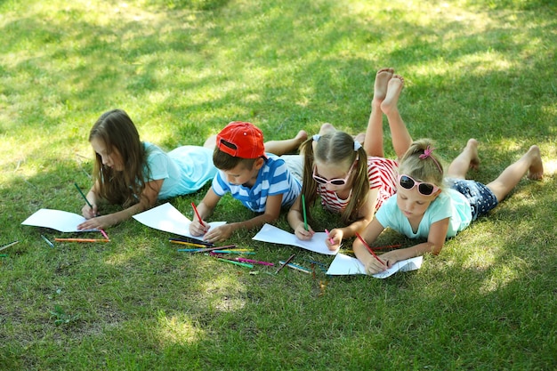 Happy active children lying on green grass and drawing in park