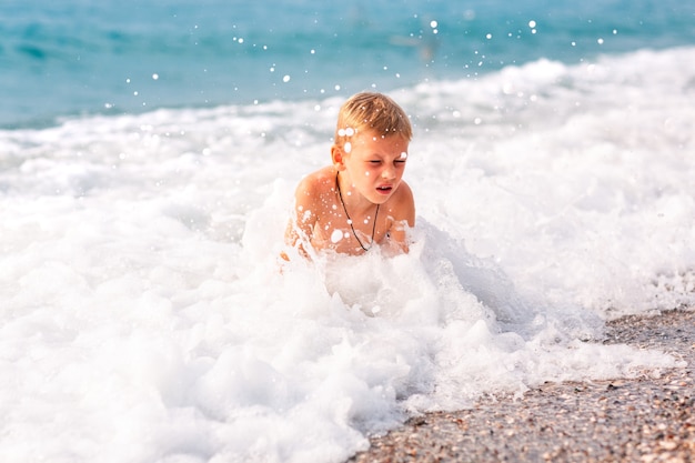 Happy active little boy having fun in the waves at the seaside