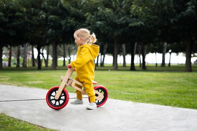 Happy active pretty cute caucasian blonde baby girl kid toddlersmiling child about 2 years old wearing bright yellow jumpers learning riding run balance bike in summer park outdoors