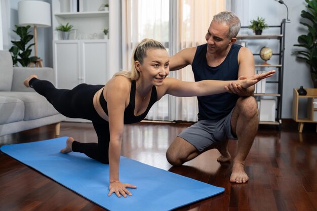 Photo happy active senior couple in sportswear being supportive and assist on yoga posture together at home healthy senior man and woman lifestyle with yoga exercise clout