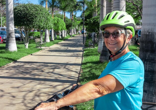 Happy active senior woman with helmet cycling in the public park with electric bicycle enjoying freedom Concept of healthy lifestyle and sustainable mobility