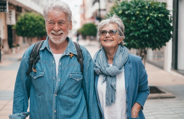 Happy active smiling adult Caucasian senior couple walking in city street