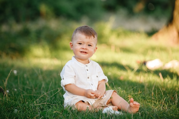 Счастливый очаровательный мальчик сидит на траве в парке