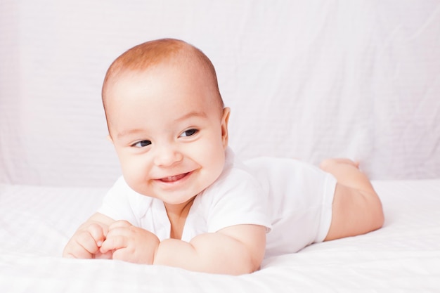 Счастливый прелестный ребенок лежит на белой кровати и улыбается