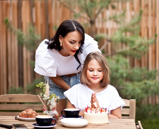 ママと幸せな愛らしい女の子は、カフェテラスでバースデーケーキで祝います。 10歳は誕生日を祝います。
