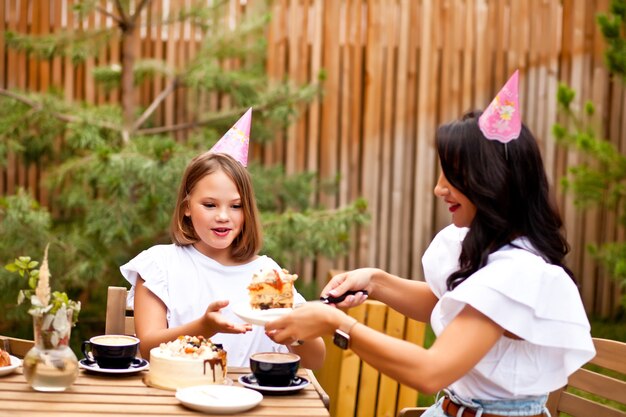 Happy adorable girl with mom celebrate with birthday cake in cafe terrace. 10 year old celebrate birthday.