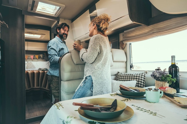 Happy adult couple enjoy vacation on camper van and prepare\
lunch together alternative travel lifestyle for modern people man\
and woman smile inside motor home van life and holiday trip\
vacation